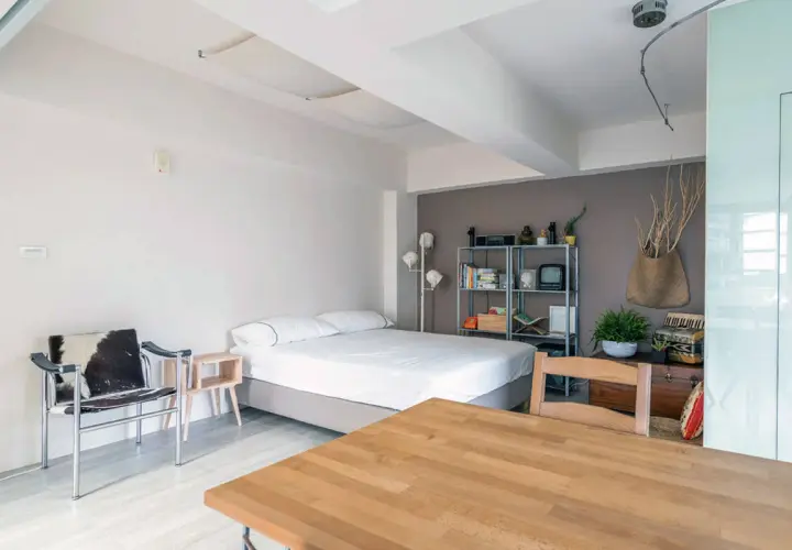 Acogedor espacio en apartamentos o estudios con cama, silla de diseño y mesa de madera.