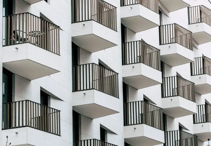Fachada moderna de edificio con balcones escalonados. Cada balcón tiene una barandilla de metal y una mesa con sillas, ideal para una cuenta vivienda.