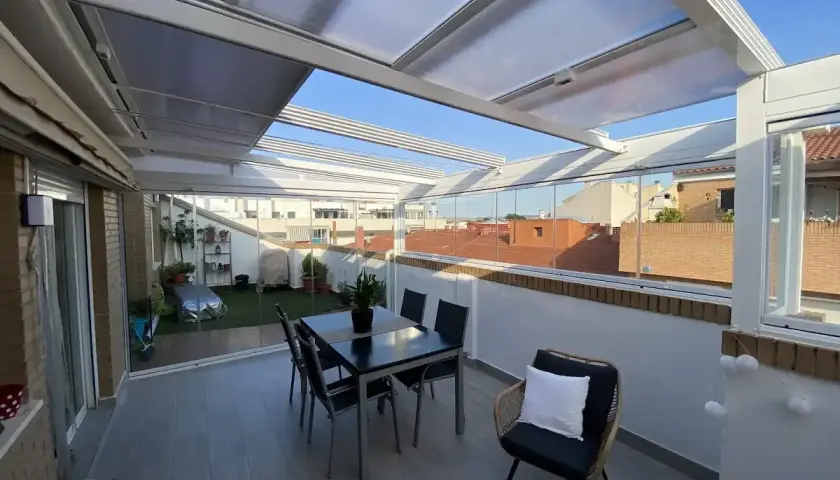 Cerramiento terraza casa unifamiliar con mesa y sillas, y zona ajardinada. Disfruta del exterior todo el año.