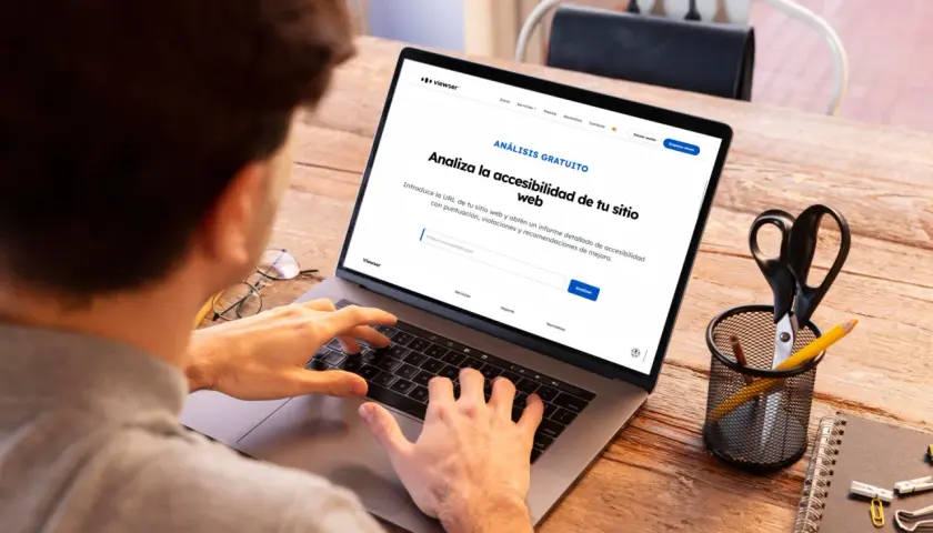 Persona usando laptop para obtener un informe de accesibilidad web. La pantalla muestra "Analiza la accesibilidad de tu sitio web".