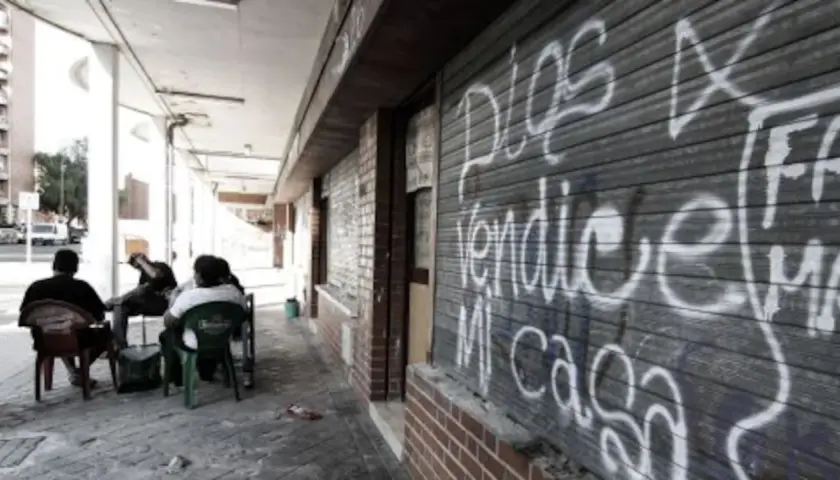 Gente sentada en sillas de plástico frente a un local con grafitis, reflejo de los peores barrios de Madrid.