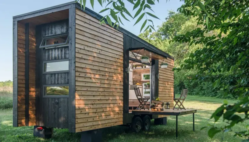 Casa móvil moderna de madera, ideal para quienes buscan qué se puede construir en terreno rústico. Tiene una terraza desplegable y está rodeada de vegetación.