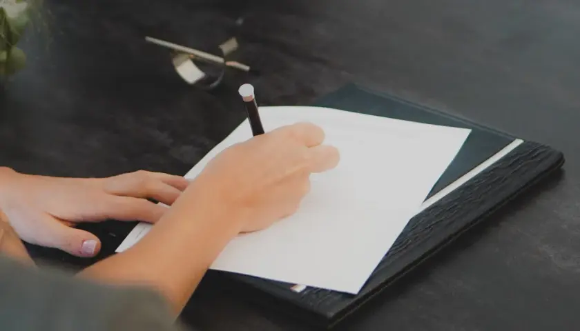 Mano escribiendo en un documento. Cualquier persona interesada en saber quién puede pedir una nota simple, puede hacerlo para verificar información.