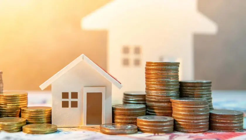 Casas pequeñas y pilas de monedas, sugiriendo ahorro para la transferencia OMF compraventa de una vivienda.