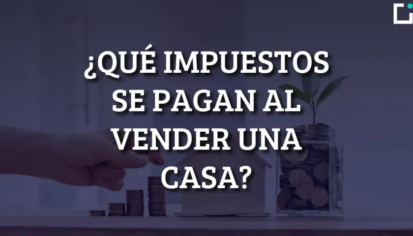 ¿Qué impuestos se pagan al vender una casa? Mano colocando monedas en una alcancía con una casa de madera y una planta.