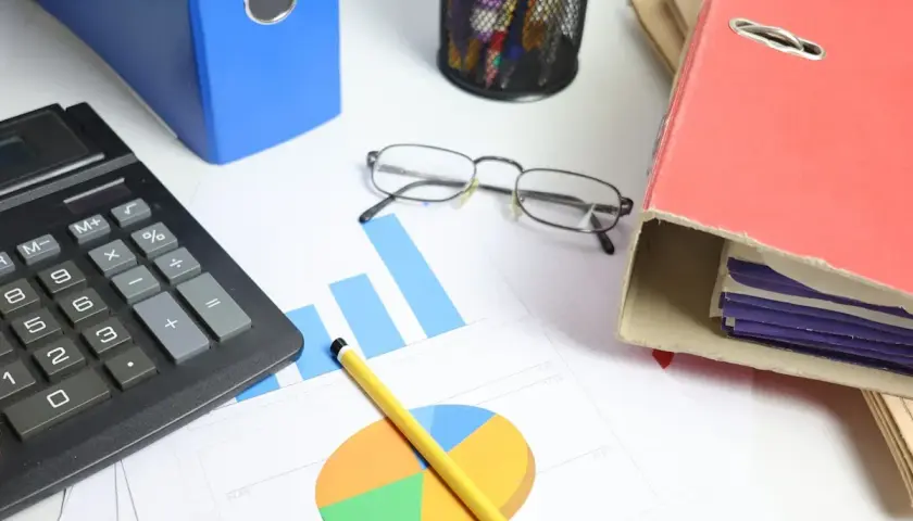 Calculadora, gráficos y carpetas sobre un escritorio. Analizando el tipo de interés actual para tomar decisiones financieras.