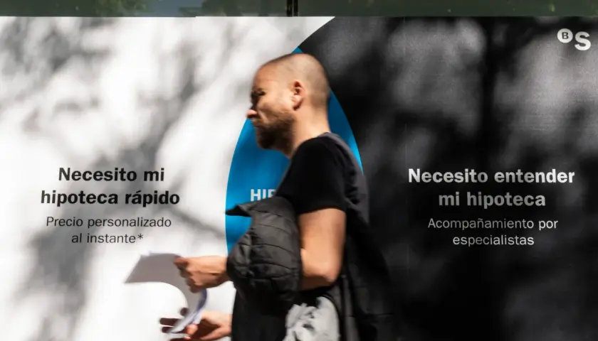 Hombre pasa frente a un anuncio que dice "Necesito mi hipoteca rápido" y "Necesito entender mi hipoteca". Pregunta: ¿quién paga el levantamiento de hipoteca?