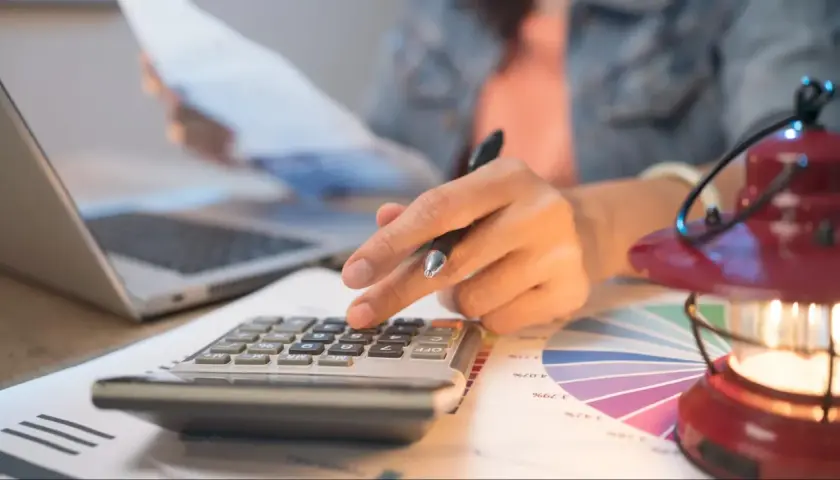 Persona calcula con calculadora y portátil, revisando gráficos. Quizás planeando una hipoteca puente Santander.