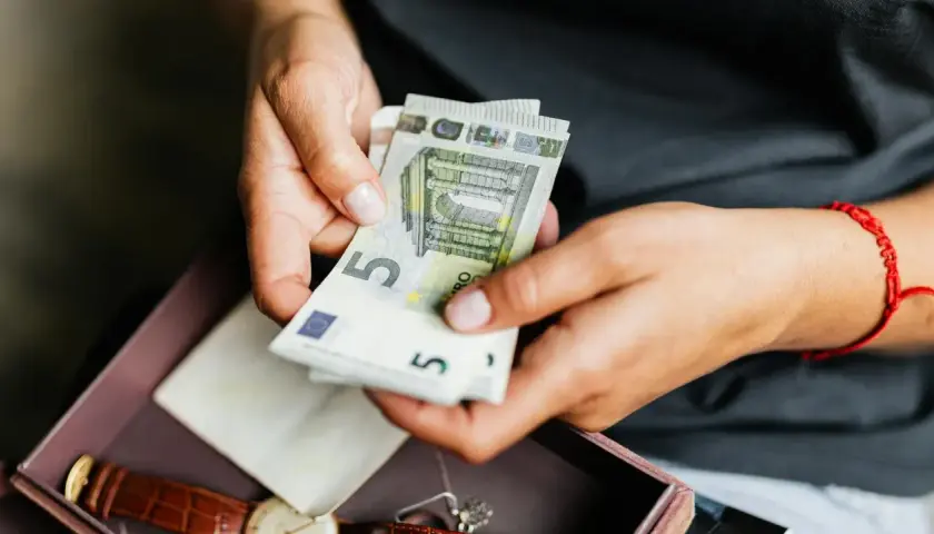 Manos contando billetes de 5 euros. No pagues la comunidad o te pueden quitar la casa.