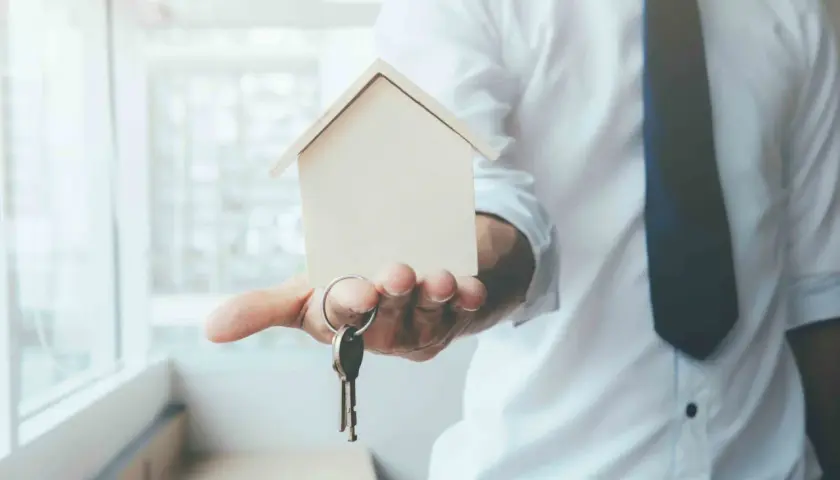 Un hombre con camisa blanca y corbata oscura ofrece una maqueta de casa y llaves, simbolizando el usufructo de una vivienda.