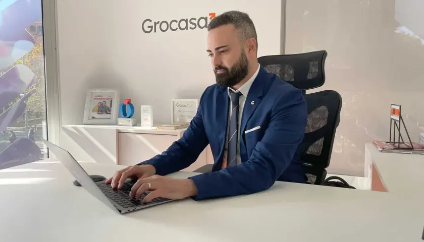 Hombre de negocios trabajando en su portátil en una oficina con el logo de Grocasa. Busca opiniones sobre Grocasa para su próximo proyecto.