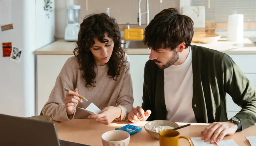 Pareja revisando facturas y usando calculadora, gestionando su comunidad de bienes entre familiares.