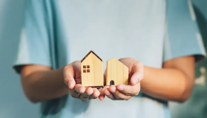 Manos sostienen dos casas de madera, como si fueran un expediente de dominio.