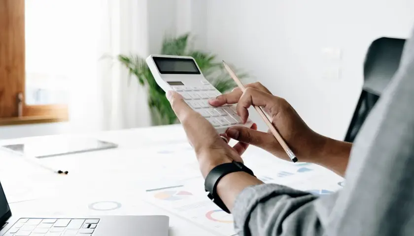 Persona calcula el valor tasación vivienda a efectos del seguro con calculadora y lápiz sobre gráficos.
