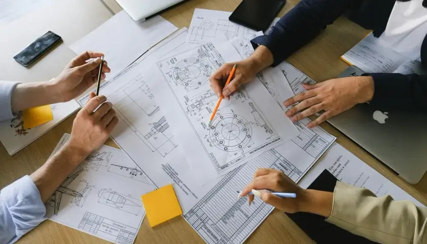 Manos revisando planos técnicos, un **informe pericial vivienda** en proceso.