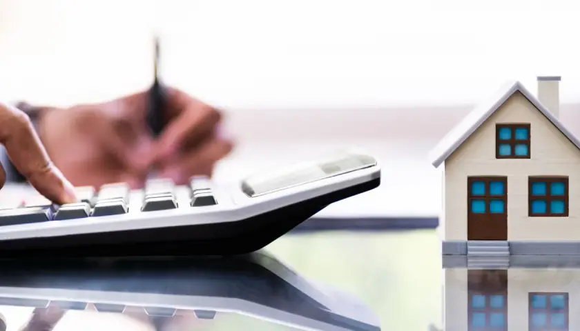 Un tasador homologado calcula el valor de una casa modelo con una calculadora.