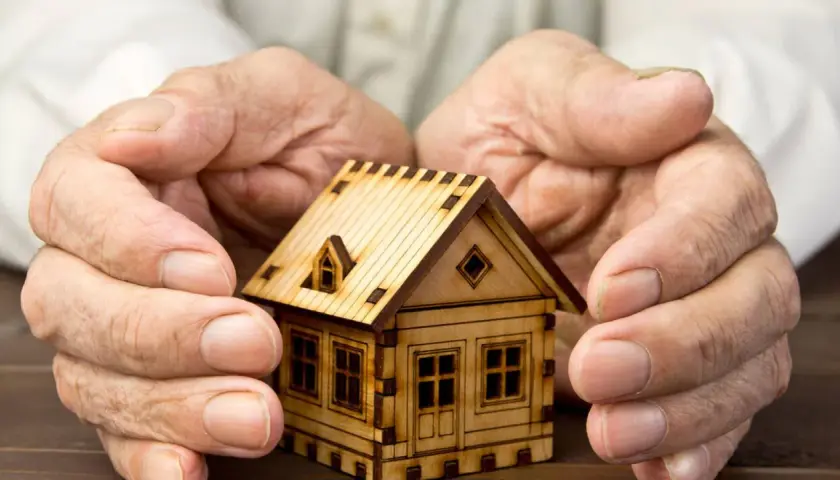 Manos protegen una maqueta de casa, simbolizando el usufructo del 50% de una vivienda.