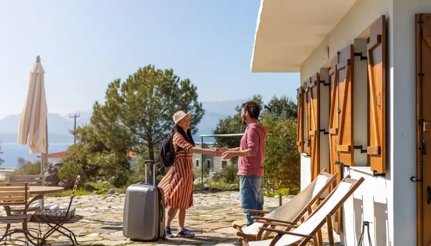 Pareja sonriendo y dándose la mano, con maleta lista para una permuta de viviendas entre particulares. Vacaciones soleadas.