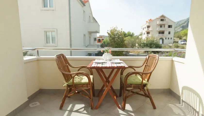 Balcón con mesa y sillas de mimbre, vistas a edificios con ventanas y balcones, elementos comunes de un edificio.
