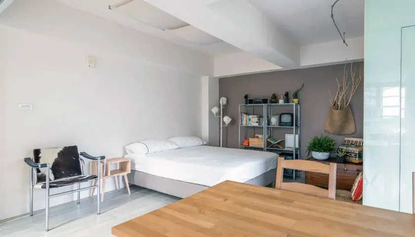 Acogedor espacio en apartamentos o estudios con cama, silla de diseño y mesa de madera.