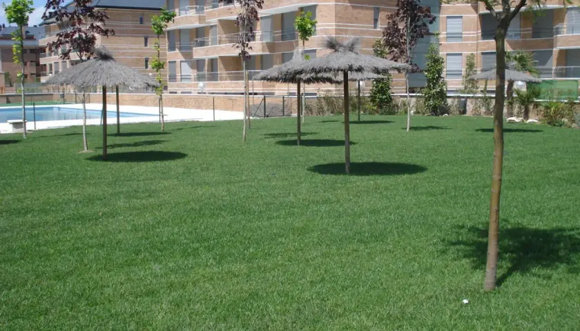 Área verde con sombrillas de paja y piscina, elementos comunes de una urbanización, regidos por la ley de propiedad horizontal.