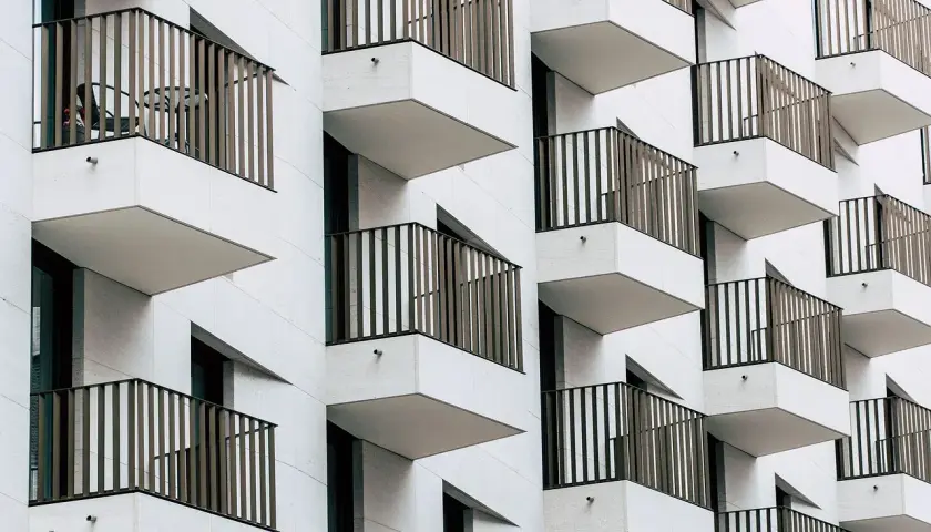 Fachada moderna de edificio con balcones escalonados. Cada balcón tiene una barandilla de metal y una mesa con sillas, ideal para una cuenta vivienda.