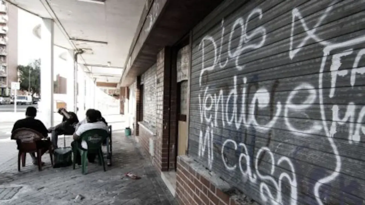 Gente sentada en sillas de plástico frente a un local con grafitis, reflejo de los peores barrios de Madrid.