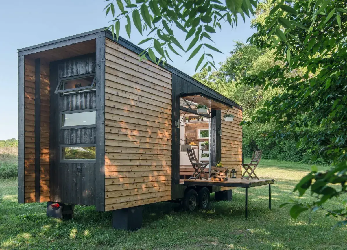 Casa móvil moderna de madera, ideal para quienes buscan qué se puede construir en terreno rústico. Tiene una terraza desplegable y está rodeada de vegetación.