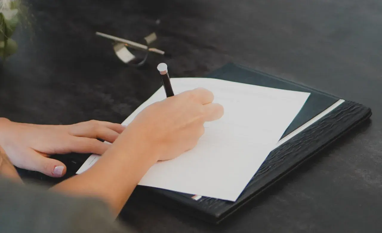Mano escribiendo en un documento. Cualquier persona interesada en saber quién puede pedir una nota simple, puede hacerlo para verificar información.
