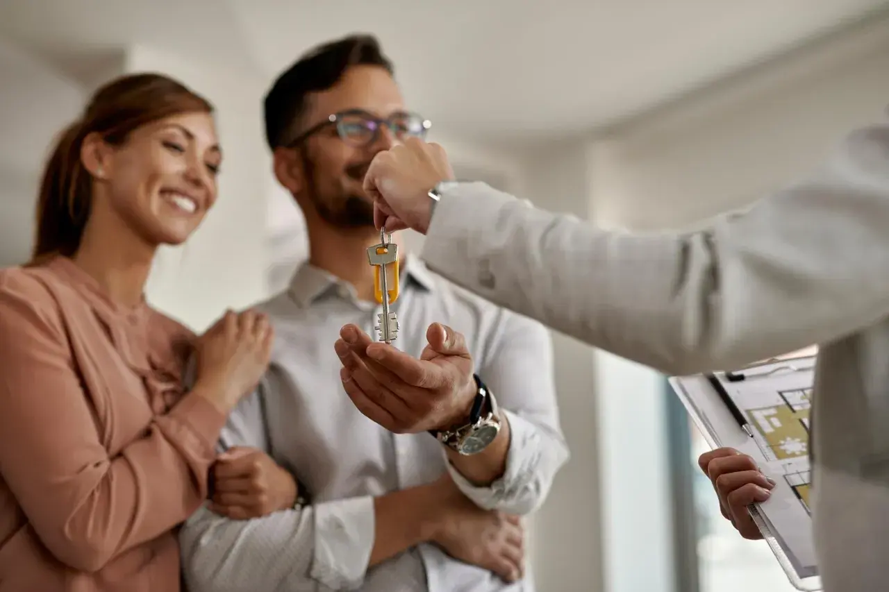 Pareja feliz recibe llaves de su nuevo hogar, superando los problemas de alquiler con opción a compra.