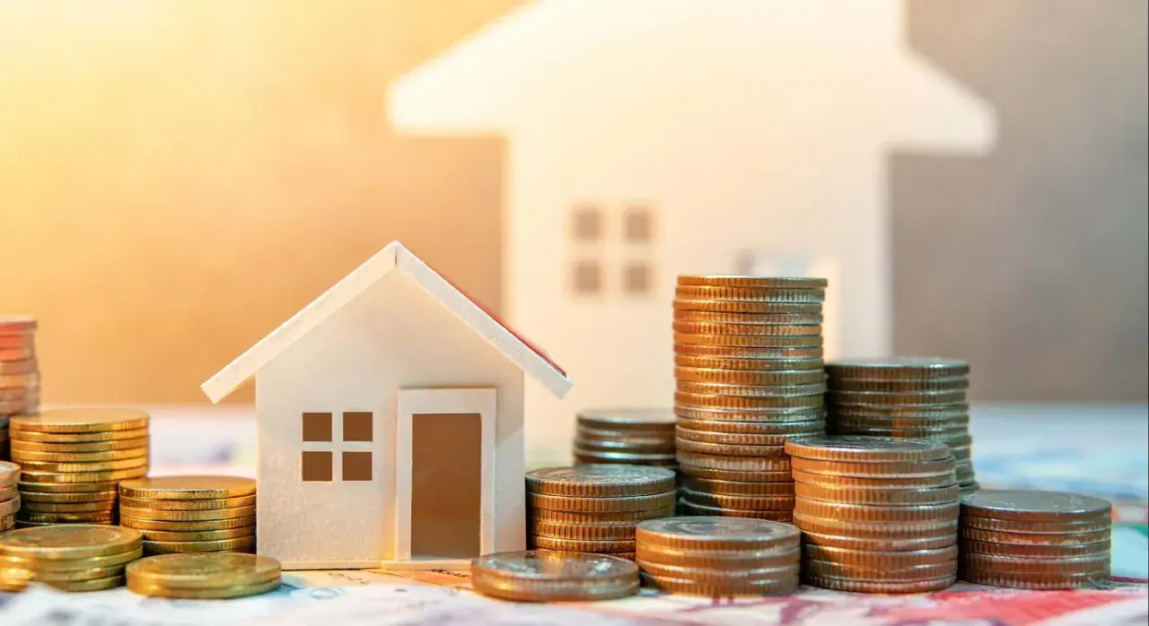 Casas pequeñas y pilas de monedas, sugiriendo ahorro para la transferencia OMF compraventa de una vivienda.