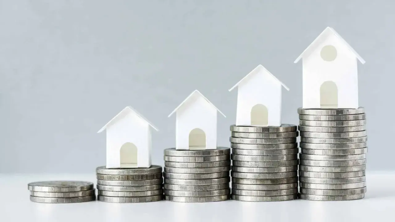 Casas blancas en pilas de monedas crecientes. Esto ilustra el concepto de LTV (Loan-to-Value) y cómo el valor de una propiedad puede aumentar con el tiempo.