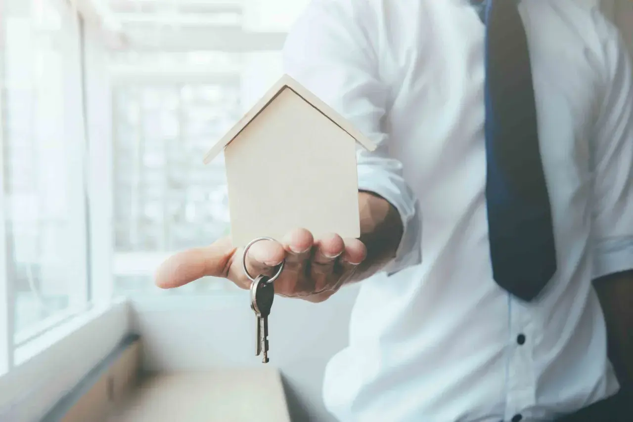 Un hombre con camisa blanca y corbata oscura ofrece una maqueta de casa y llaves, simbolizando el usufructo de una vivienda.