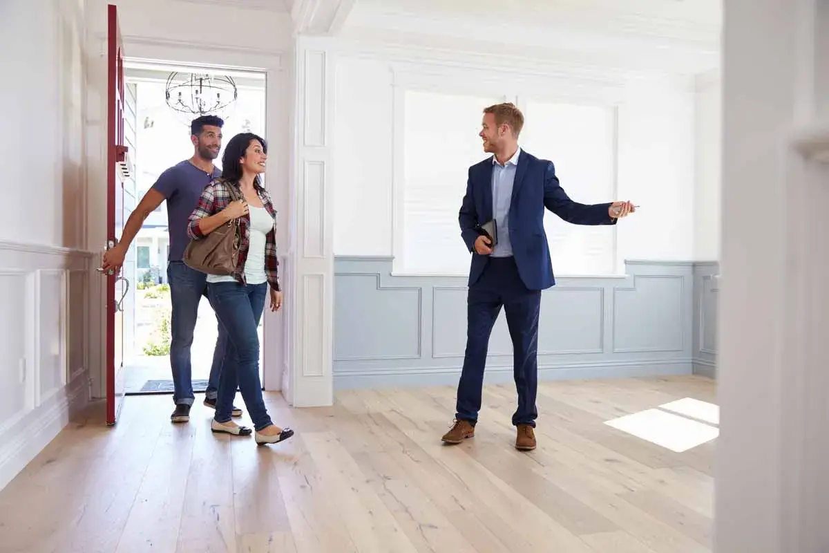 Agente inmobiliario muestra una casa a una pareja. ¿Quién paga la tasación de una hipoteca? El comprador.