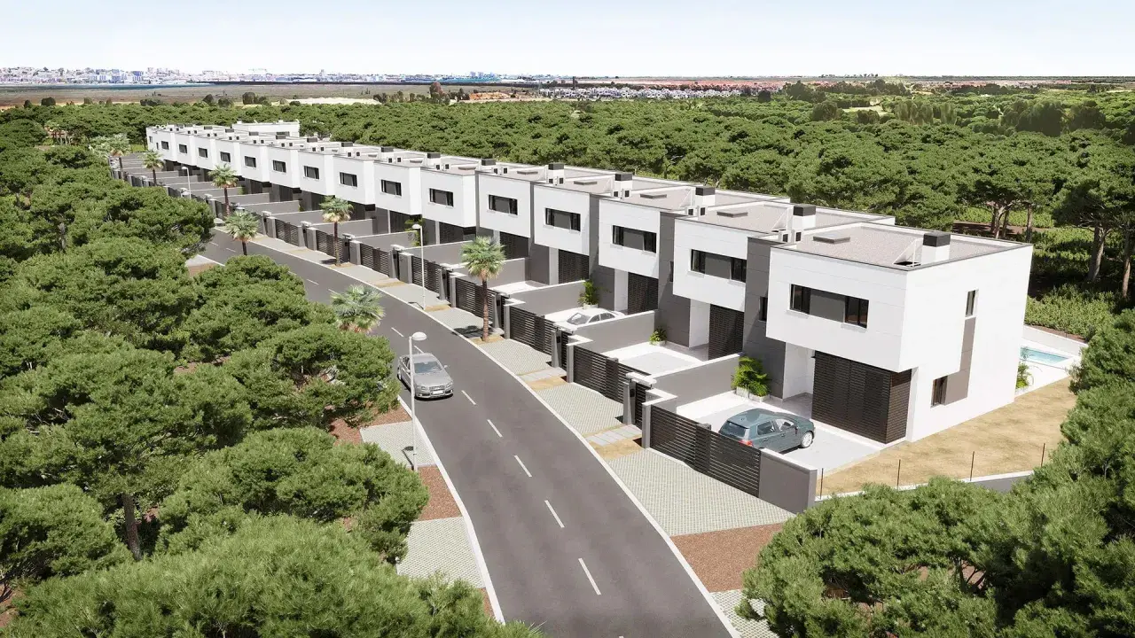Una hilera de modernos chalets pareados blancos y grises, rodeados de pinos, con una carretera y coches.