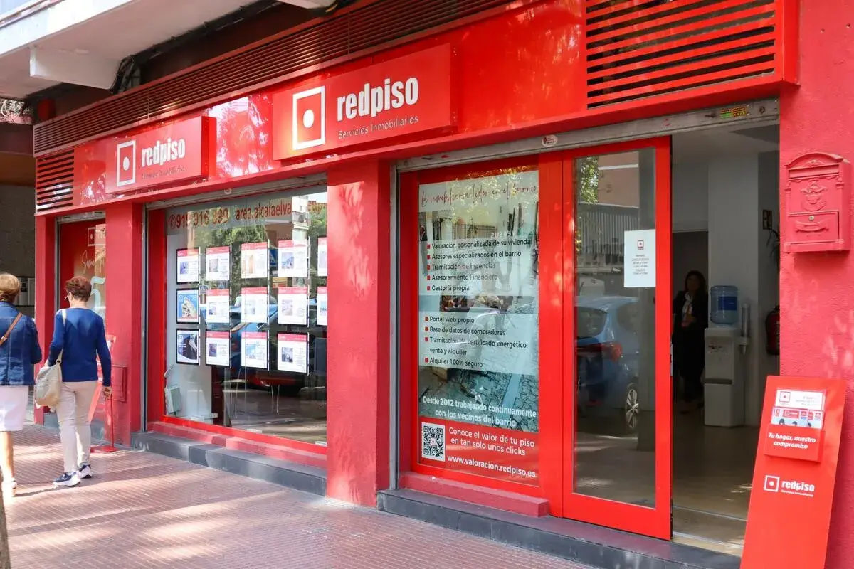 Redpiso, inmobiliaria con opiniones positivas. Fachada roja, escaparate con anuncios de pisos y dos mujeres mirando.