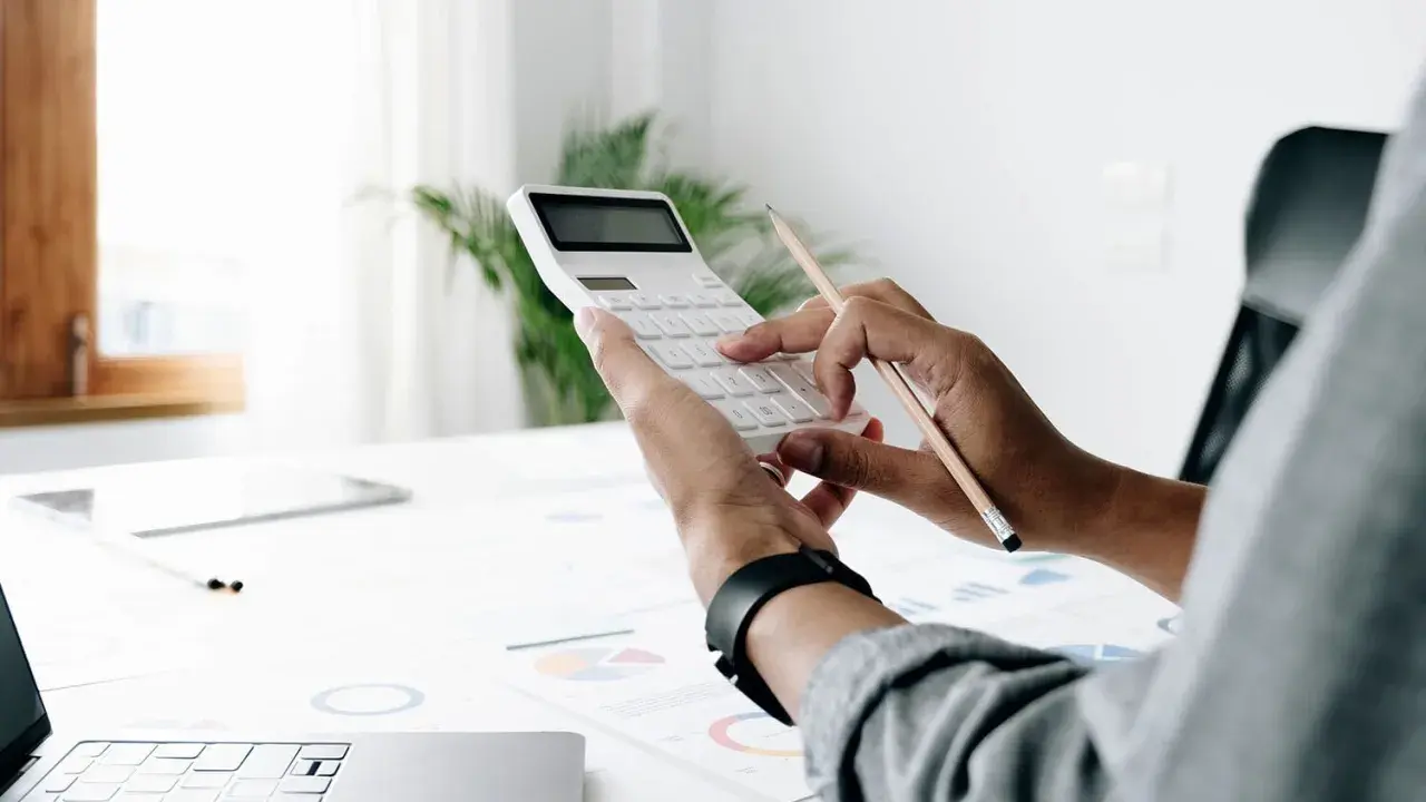 Persona calcula el valor tasación vivienda a efectos del seguro con calculadora y lápiz sobre gráficos.