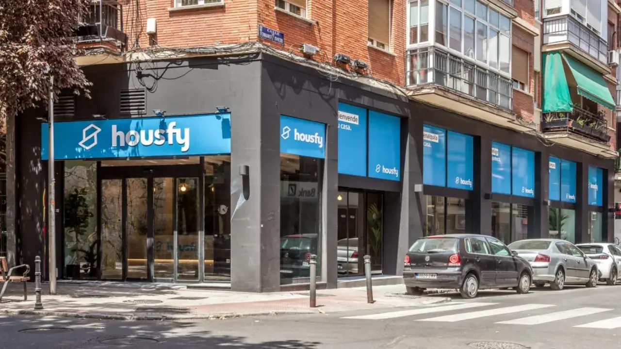 Fachada de oficina de Housfy, con letreros azules y blancos. Las opiniones sobre Housfy son positivas, como se ve en su presencia en la calle.