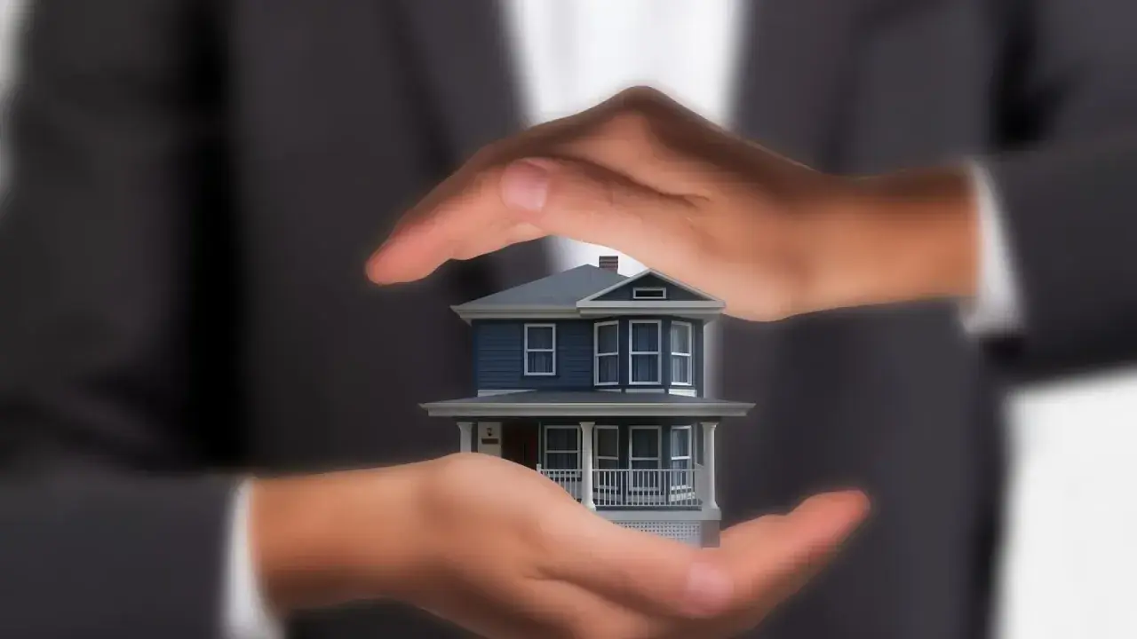 Manos protegen una maqueta de casa, simbolizando lo que se necesita para tasar una vivienda: cuidado y análisis.
