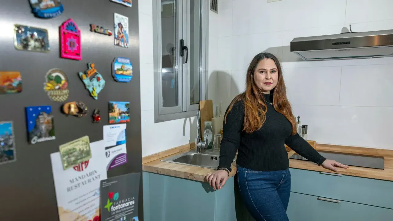 Mujer en cocina, con imanes de viajes en la nevera. Una opción para tu futuro hogar: alquiler con opción a compra entre particulares.