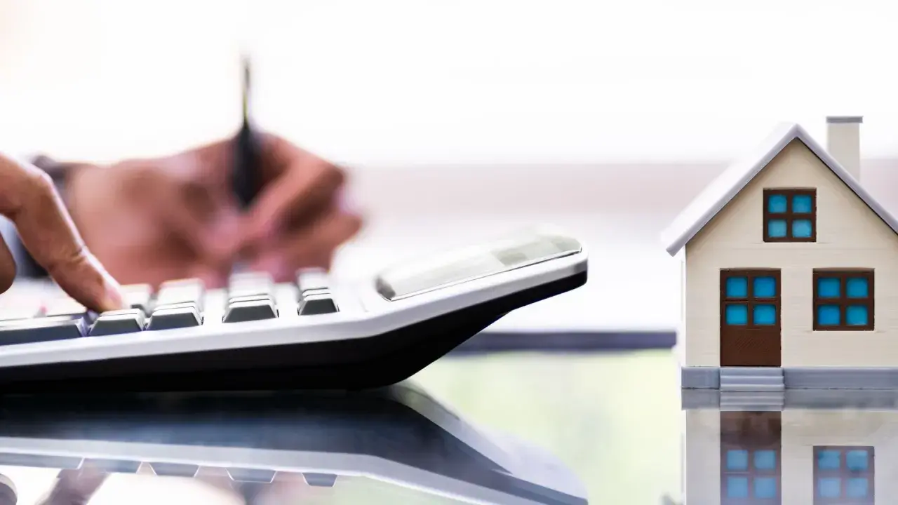 Un tasador homologado calcula el valor de una casa modelo con una calculadora.