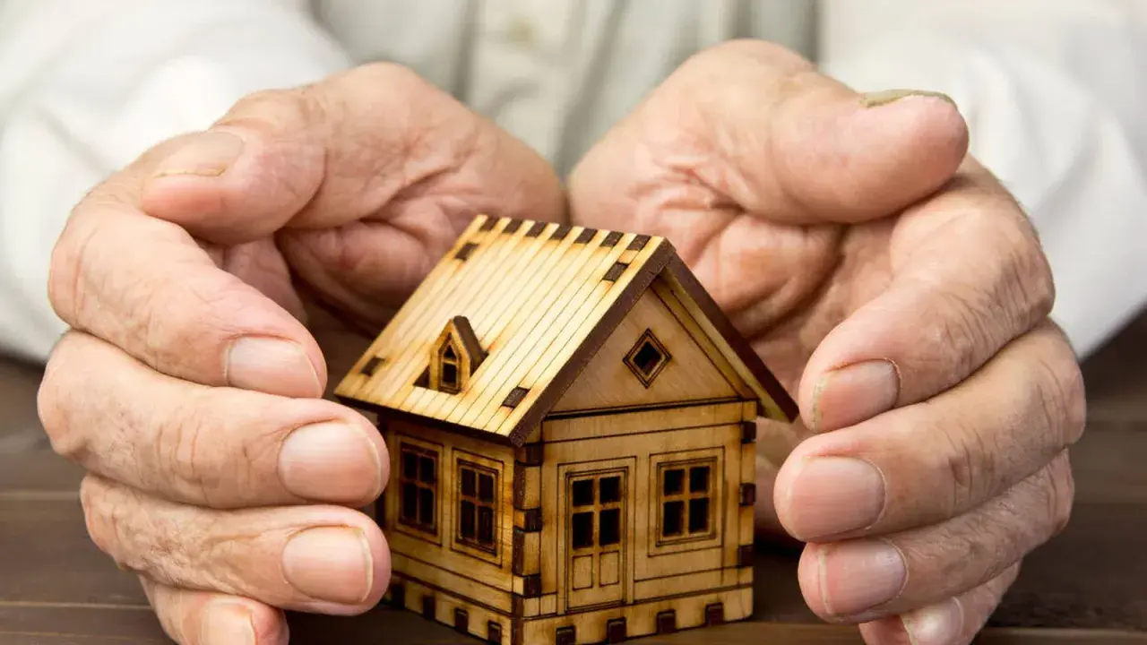 Manos protegen una maqueta de casa, simbolizando el usufructo del 50% de una vivienda.
