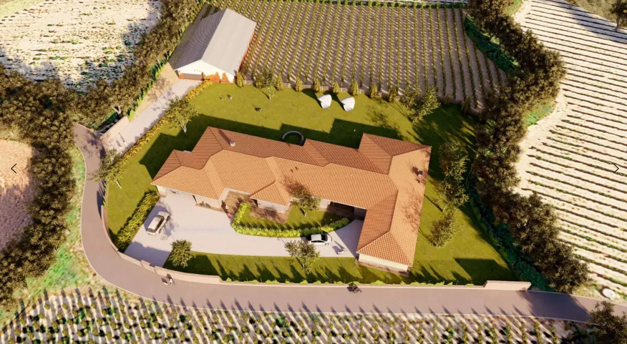 Vista aérea de una casa moderna con tejado de tejas, rodeada de viñedos y campos. Los planos de piso se visualizan en esta representación 3D.