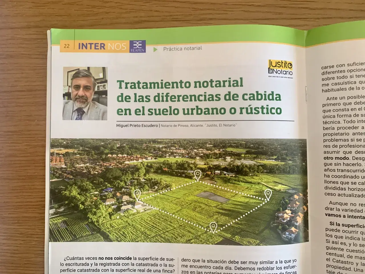 Artículo sobre el tratamiento notarial de diferencias de cabida en fincas. La imagen muestra una vista aérea de parcelas y casas, con marcadores que sugieren la delimitación de un terreno, abordando el problema del exceso de cabida.