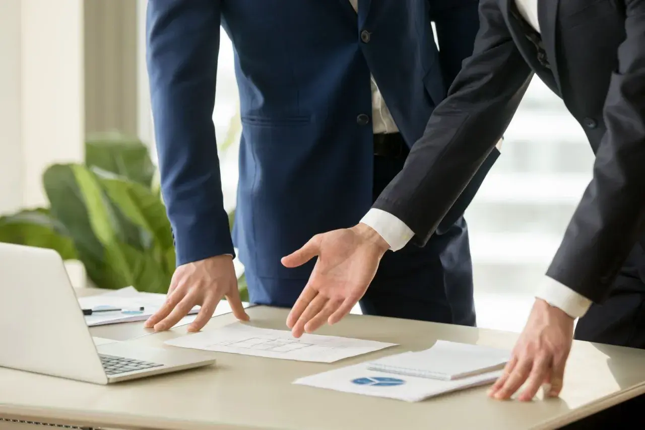 Dos hombres de negocios analizan un plano. Se discute el precio del informe pericial arquitecto.
