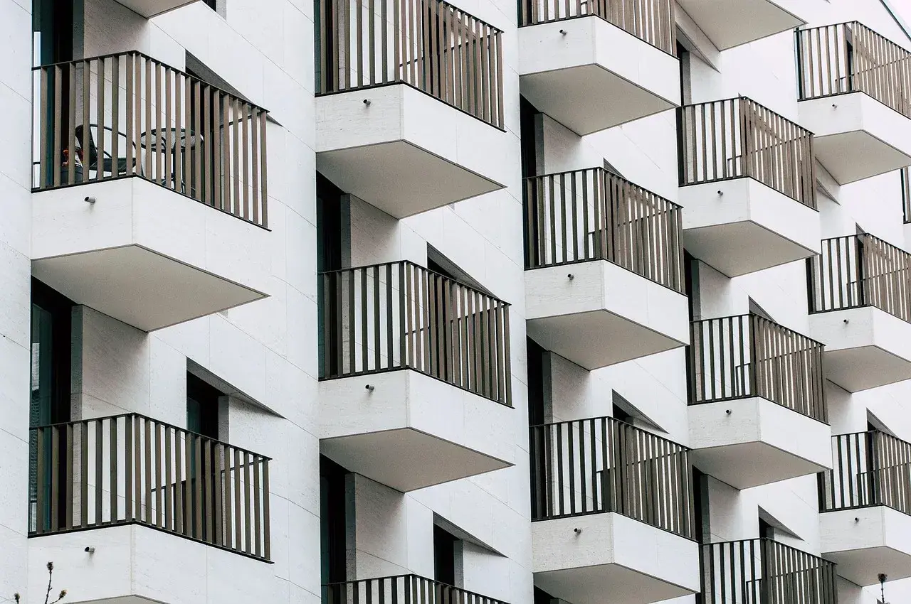 Fachada moderna de edificio con balcones escalonados. Cada balcón tiene una barandilla de metal y una mesa con sillas, ideal para una cuenta vivienda.