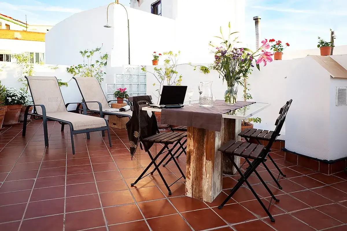 Terraza con tumbonas, mesa y sillas. Un portátil y flores decoran la mesa. Este piso es un inmueble perfecto para disfrutar del exterior.