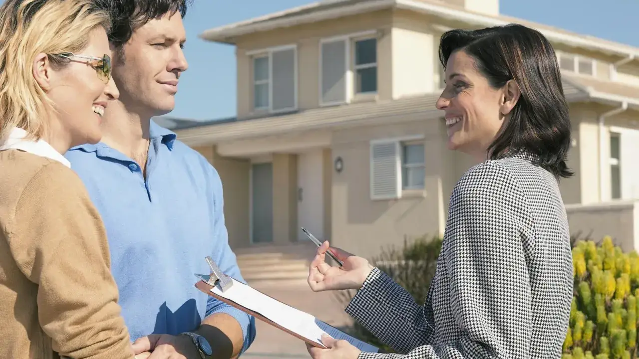 Pareja sonriente habla con agente inmobiliaria frente a su nueva casa. ¡Excelentes huspy opiniones!