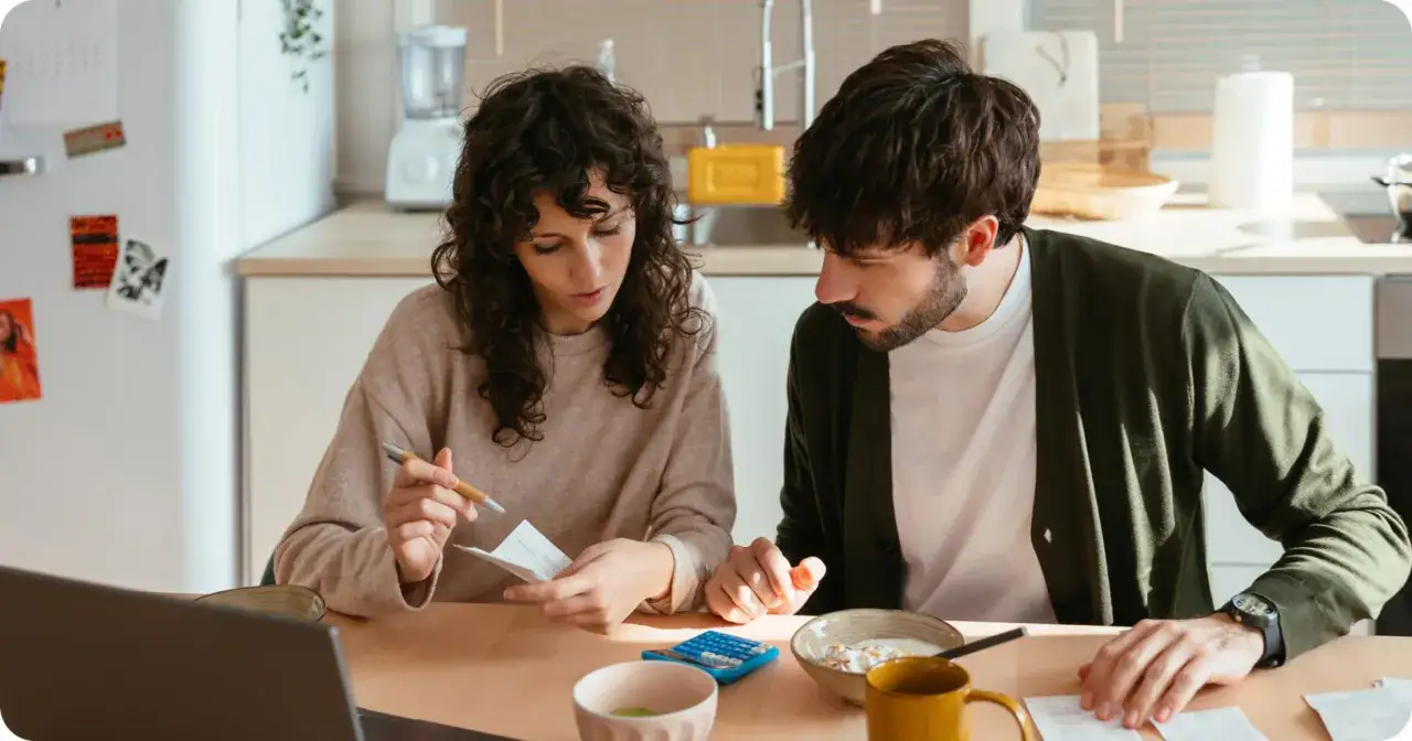 Pareja revisando facturas y usando calculadora, planificando su comunidad de bienes entre familiares.