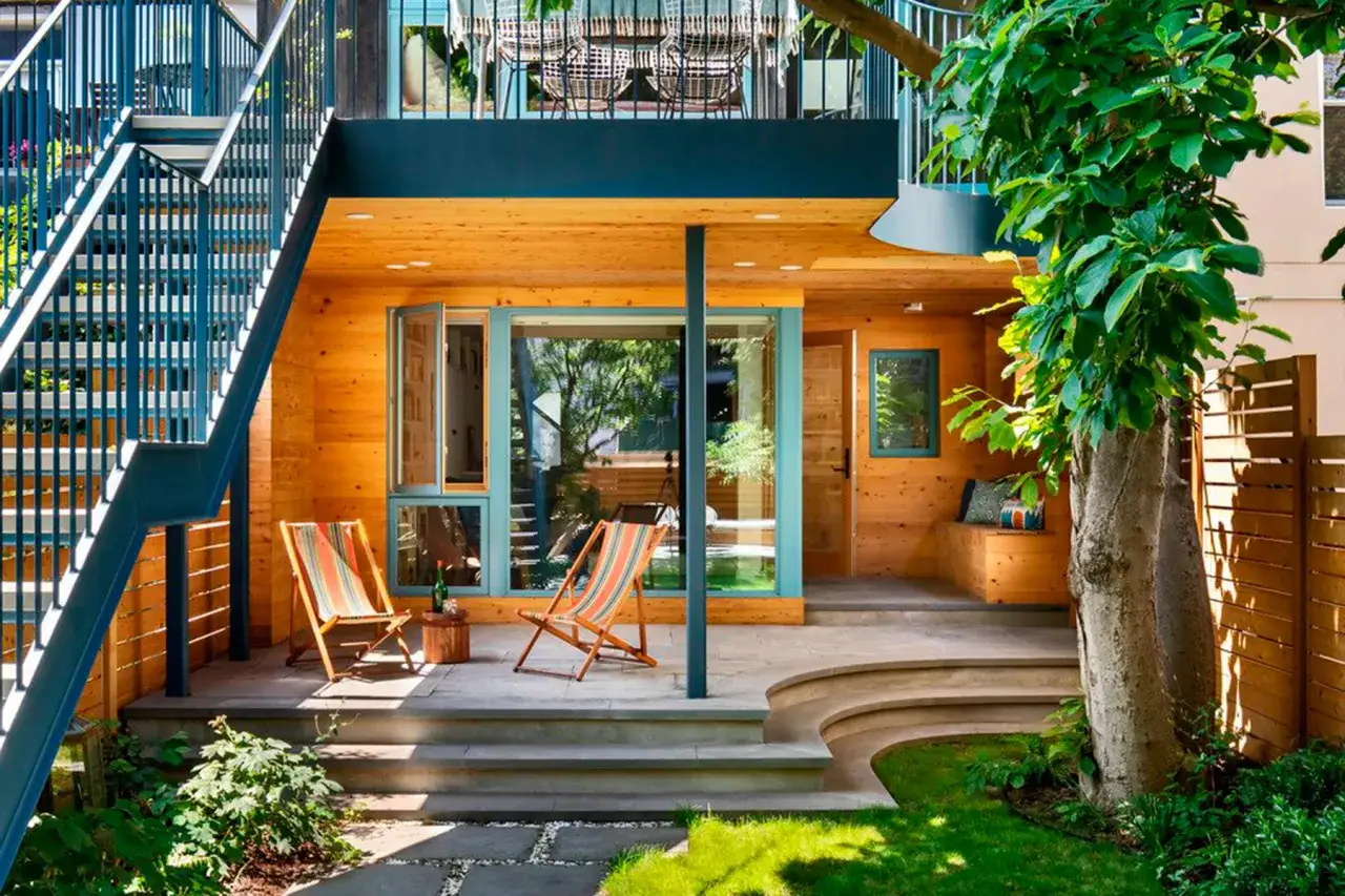 Modern chalet pareado con escaleras exteriores azules, terraza de madera y césped verde.